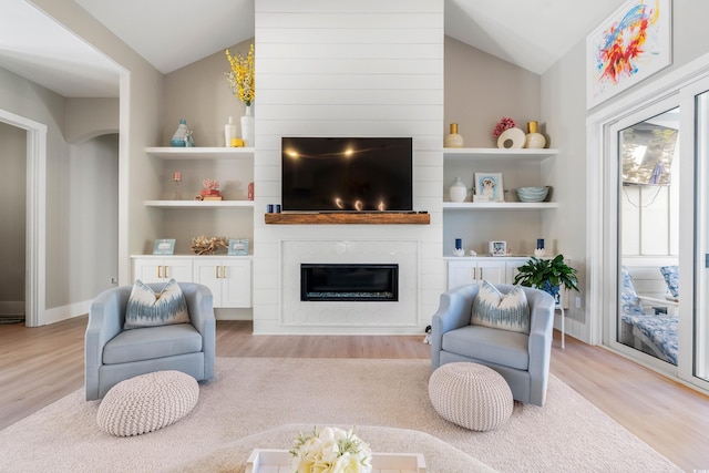 living room featuring lofted ceiling, a large fireplace, and light wood-type flooring