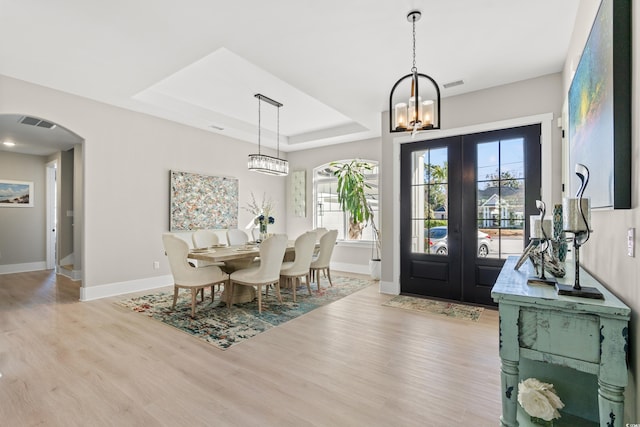 dining area featuring an inviting chandelier, a raised ceiling, light hardwood / wood-style floors, and french doors