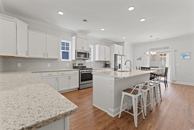 kitchen featuring crown molding, white cabinets, decorative light fixtures, an island with sink, and stainless steel appliances