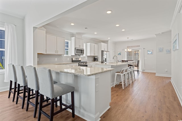 kitchen with appliances with stainless steel finishes, a kitchen island, white cabinetry, hanging light fixtures, and a breakfast bar area