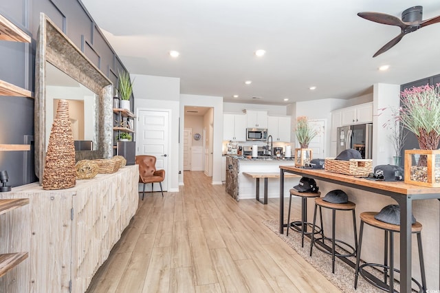 kitchen featuring appliances with stainless steel finishes, white cabinetry, ceiling fan, light hardwood / wood-style flooring, and a breakfast bar area