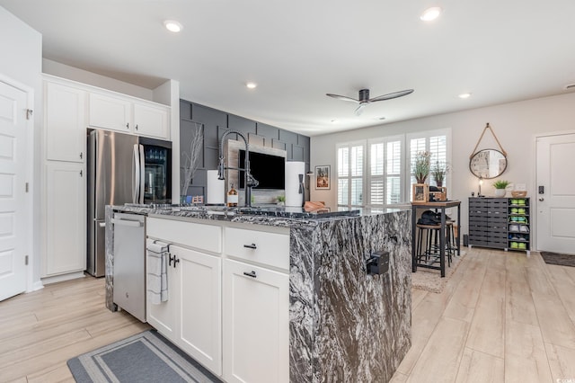 kitchen with white cabinetry, light hardwood / wood-style flooring, a kitchen island with sink, and dark stone counters