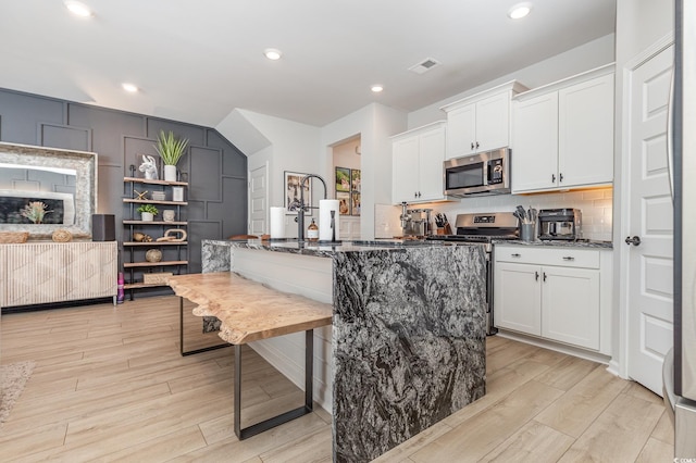 kitchen featuring an island with sink, white cabinets, dark stone countertops, and stainless steel appliances