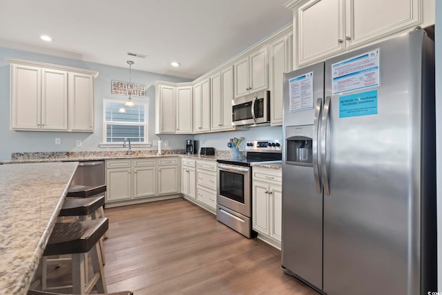 kitchen featuring wood-type flooring, sink, decorative light fixtures, stainless steel appliances, and light stone counters