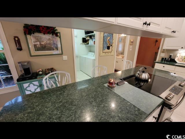 kitchen with white cabinetry, washer and clothes dryer, and stainless steel range with electric stovetop