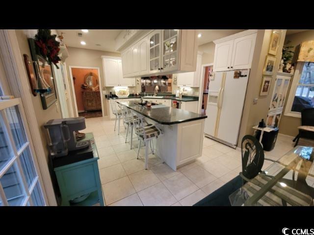 kitchen with white cabinetry, light tile patterned floors, a kitchen breakfast bar, a kitchen island, and white refrigerator with ice dispenser