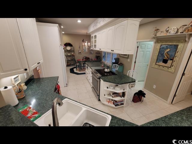 kitchen featuring sink, electric range, light tile patterned floors, and white cabinets