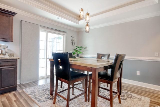 dining space with light hardwood / wood-style floors, crown molding, and a raised ceiling