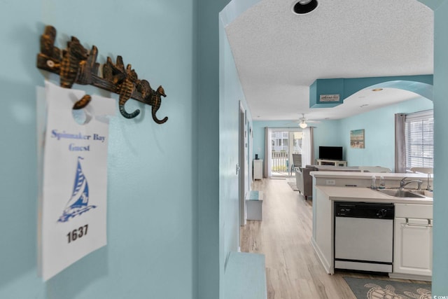 kitchen with a textured ceiling, dishwasher, white cabinets, sink, and light hardwood / wood-style flooring