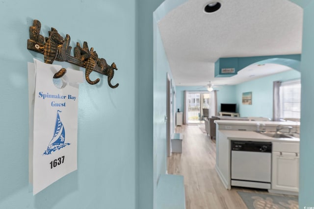 hallway with light wood-type flooring, a textured ceiling, and sink