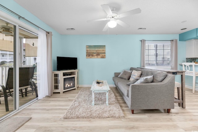 living room with light wood-type flooring, ceiling fan, and a textured ceiling