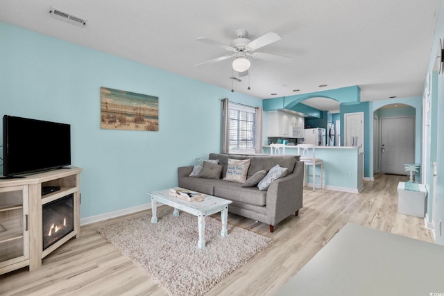 living room with light hardwood / wood-style floors, a textured ceiling, and ceiling fan