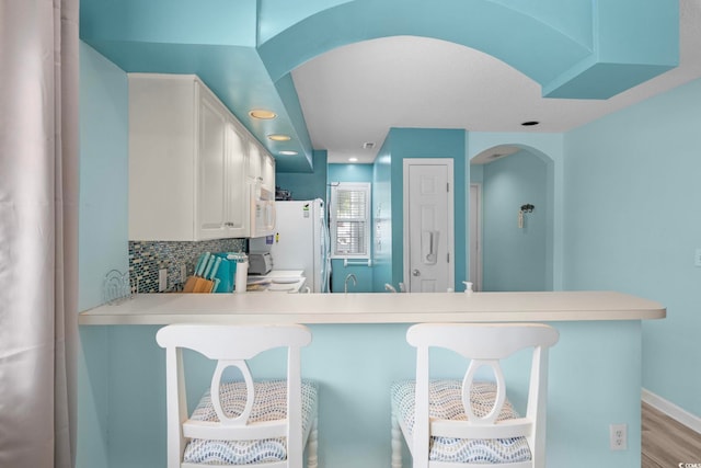 kitchen with kitchen peninsula, tasteful backsplash, a breakfast bar area, and white cabinetry