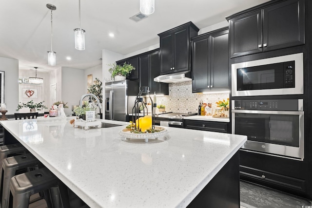 kitchen featuring decorative light fixtures, backsplash, appliances with stainless steel finishes, and a spacious island