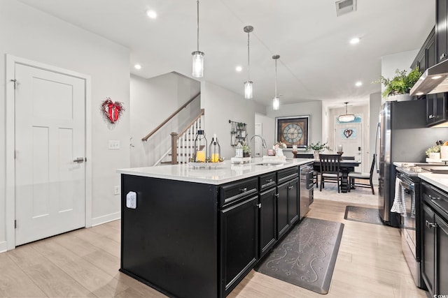 kitchen featuring light hardwood / wood-style flooring, pendant lighting, appliances with stainless steel finishes, sink, and a kitchen island with sink