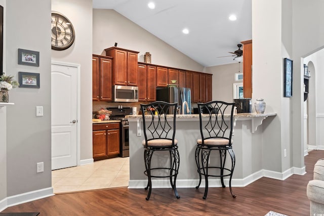 kitchen with a kitchen bar, light stone countertops, kitchen peninsula, backsplash, and stainless steel appliances