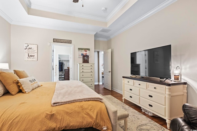 bedroom featuring crown molding, a tray ceiling, dark hardwood / wood-style flooring, and a walk in closet