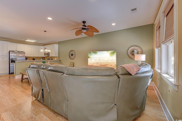 living room with ceiling fan with notable chandelier, light hardwood / wood-style flooring, and vaulted ceiling