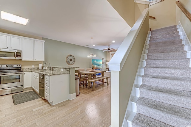 kitchen with pendant lighting, kitchen peninsula, white cabinets, and appliances with stainless steel finishes