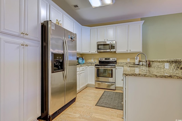 kitchen featuring sink, white cabinetry, light hardwood / wood-style flooring, appliances with stainless steel finishes, and light stone countertops