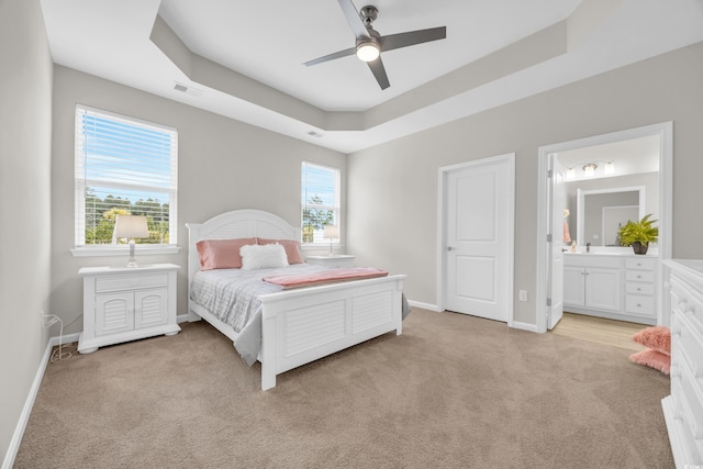 bedroom featuring a raised ceiling, ceiling fan, light colored carpet, and ensuite bath