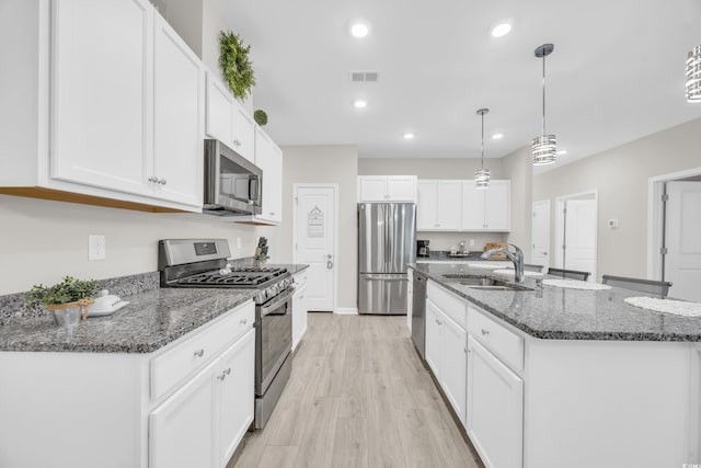 kitchen featuring decorative light fixtures, white cabinetry, sink, stainless steel appliances, and a center island with sink