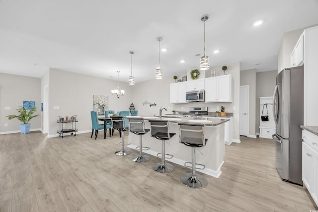 kitchen featuring white cabinetry, appliances with stainless steel finishes, decorative light fixtures, and an island with sink