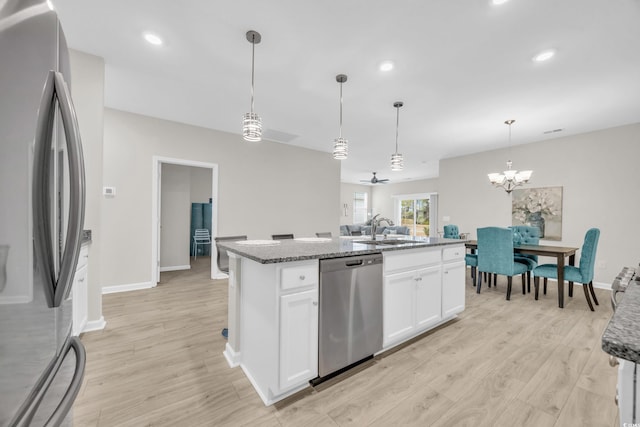 kitchen with sink, appliances with stainless steel finishes, a kitchen island with sink, hanging light fixtures, and white cabinets