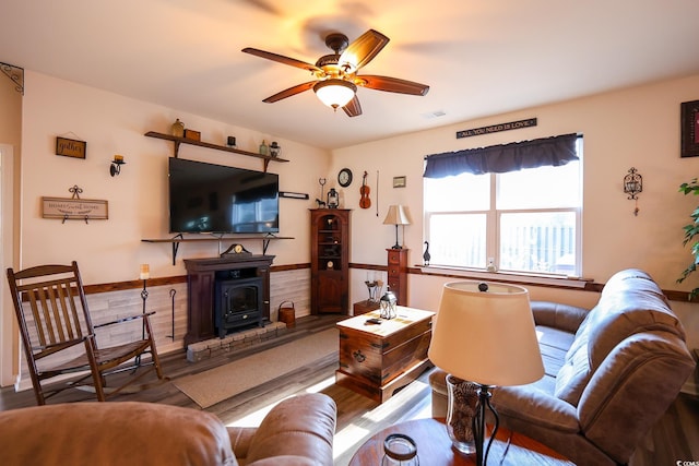 living room with ceiling fan, hardwood / wood-style floors, and a wood stove