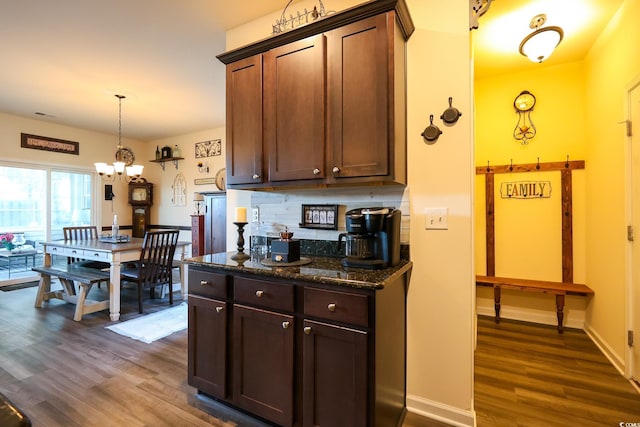 kitchen featuring backsplash, decorative light fixtures, dark wood-type flooring, and dark stone counters