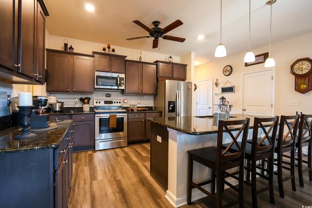 kitchen with dark stone countertops, hanging light fixtures, appliances with stainless steel finishes, and a kitchen island