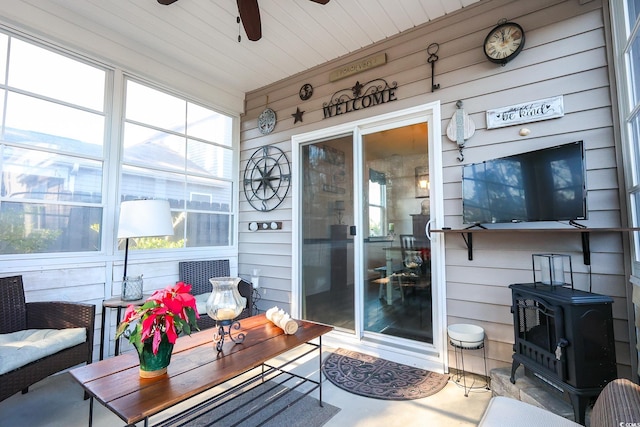 sunroom / solarium with ceiling fan and a wood stove