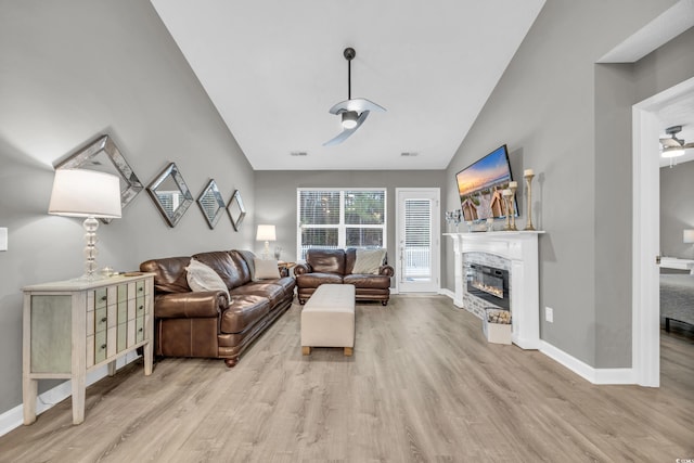 living room with a stone fireplace, vaulted ceiling, and light wood-type flooring