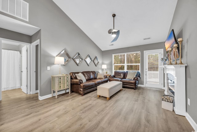 living room featuring light wood finished floors, high vaulted ceiling, baseboards, and a glass covered fireplace