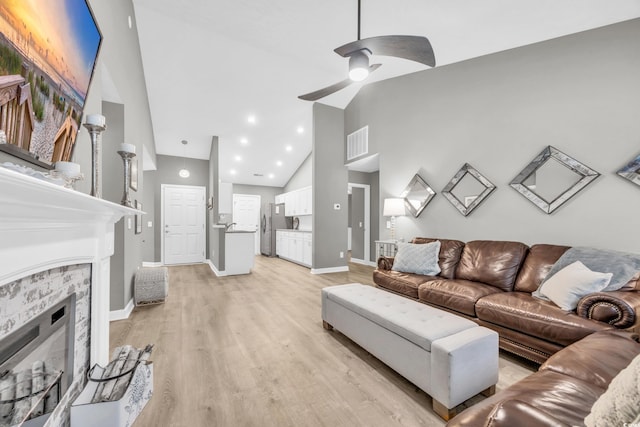 living room featuring a stone fireplace, high vaulted ceiling, ceiling fan, and light wood-type flooring