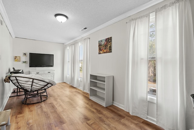 living area featuring a textured ceiling, light hardwood / wood-style flooring, crown molding, and a healthy amount of sunlight