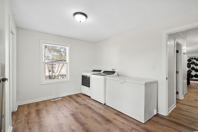 clothes washing area featuring light wood-type flooring, a textured ceiling, and washer and clothes dryer