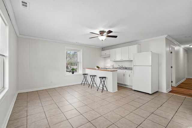 kitchen featuring white cabinets, white refrigerator, a breakfast bar, and crown molding