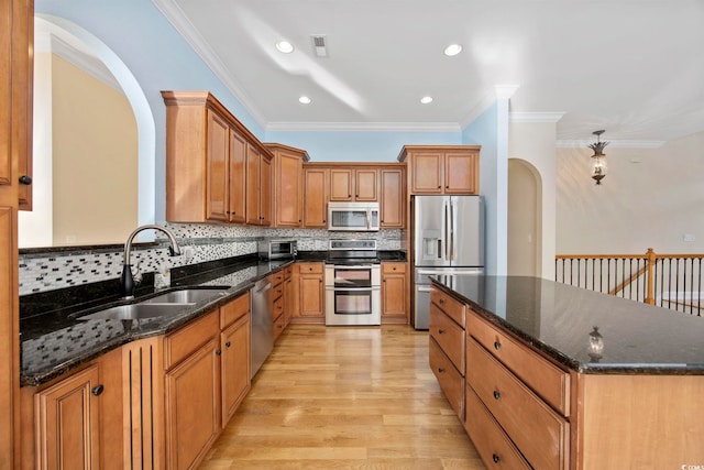 kitchen featuring sink, tasteful backsplash, dark stone counters, stainless steel appliances, and light hardwood / wood-style floors