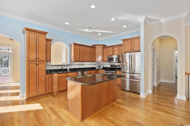 kitchen with appliances with stainless steel finishes, sink, dark stone counters, a center island, and light hardwood / wood-style floors