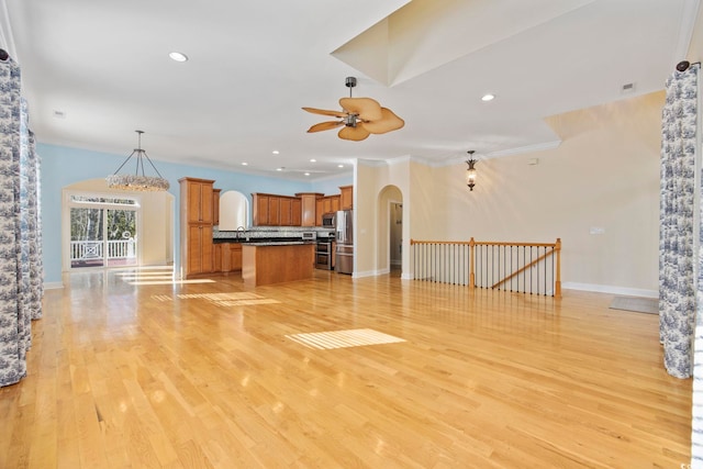 unfurnished living room featuring crown molding, ceiling fan with notable chandelier, and light hardwood / wood-style flooring