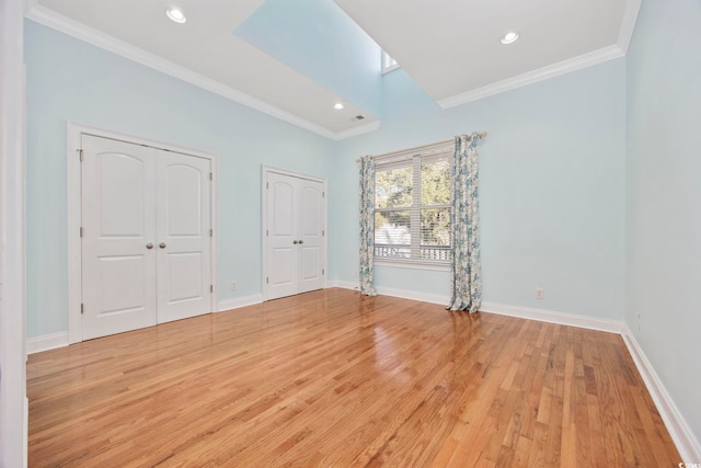 unfurnished bedroom with crown molding, multiple closets, and light wood-type flooring