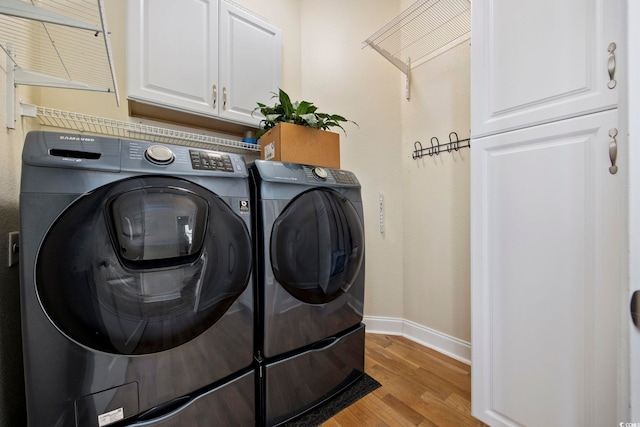 clothes washing area with washer and clothes dryer, cabinets, and light wood-type flooring