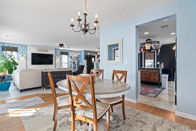 dining space with ceiling fan with notable chandelier, wood finished floors, visible vents, and baseboards