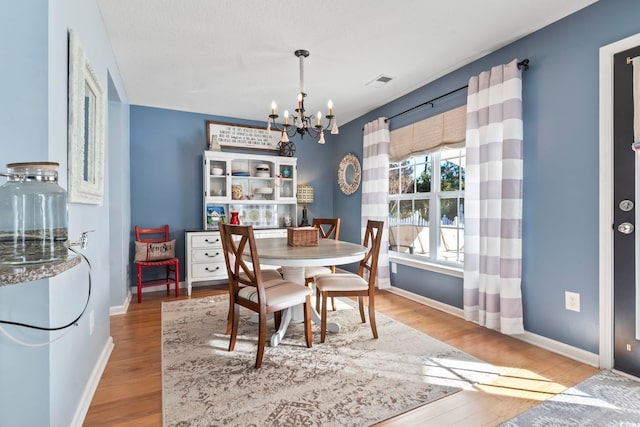 dining space featuring a chandelier, wood finished floors, visible vents, and baseboards