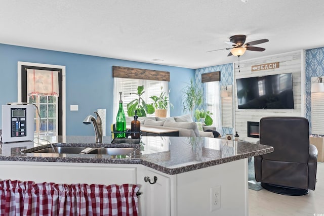 kitchen featuring a large fireplace, white cabinetry, a sink, a textured ceiling, and dark stone countertops