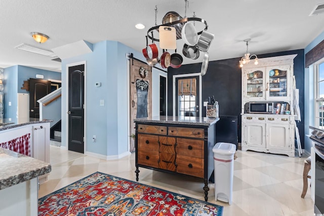 kitchen featuring visible vents, baseboards, a kitchen island, stainless steel microwave, and a chandelier