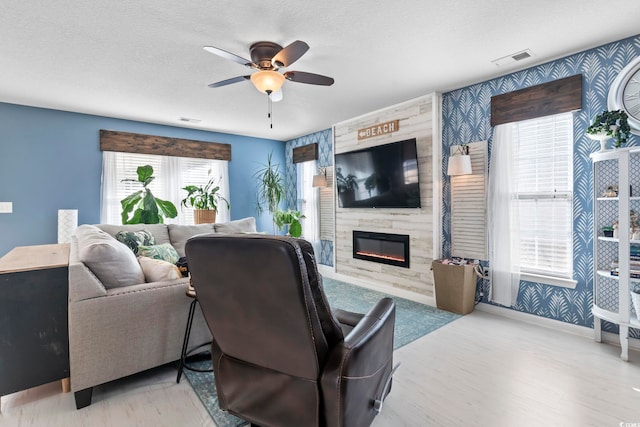 living room featuring wallpapered walls, visible vents, a ceiling fan, a textured ceiling, and a high end fireplace