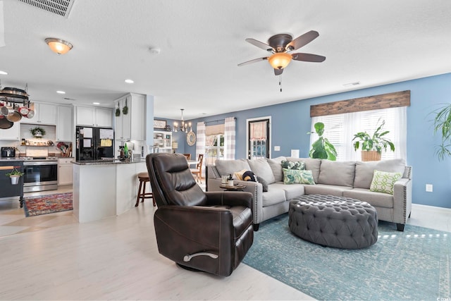 living room with ceiling fan with notable chandelier, light wood-style flooring, a textured ceiling, and visible vents