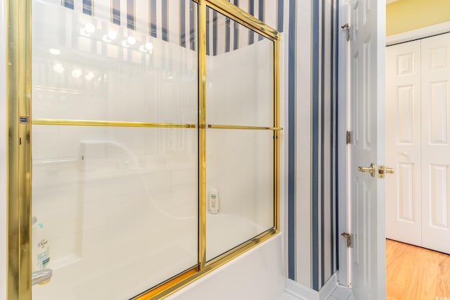 bathroom with combined bath / shower with glass door and hardwood / wood-style floors